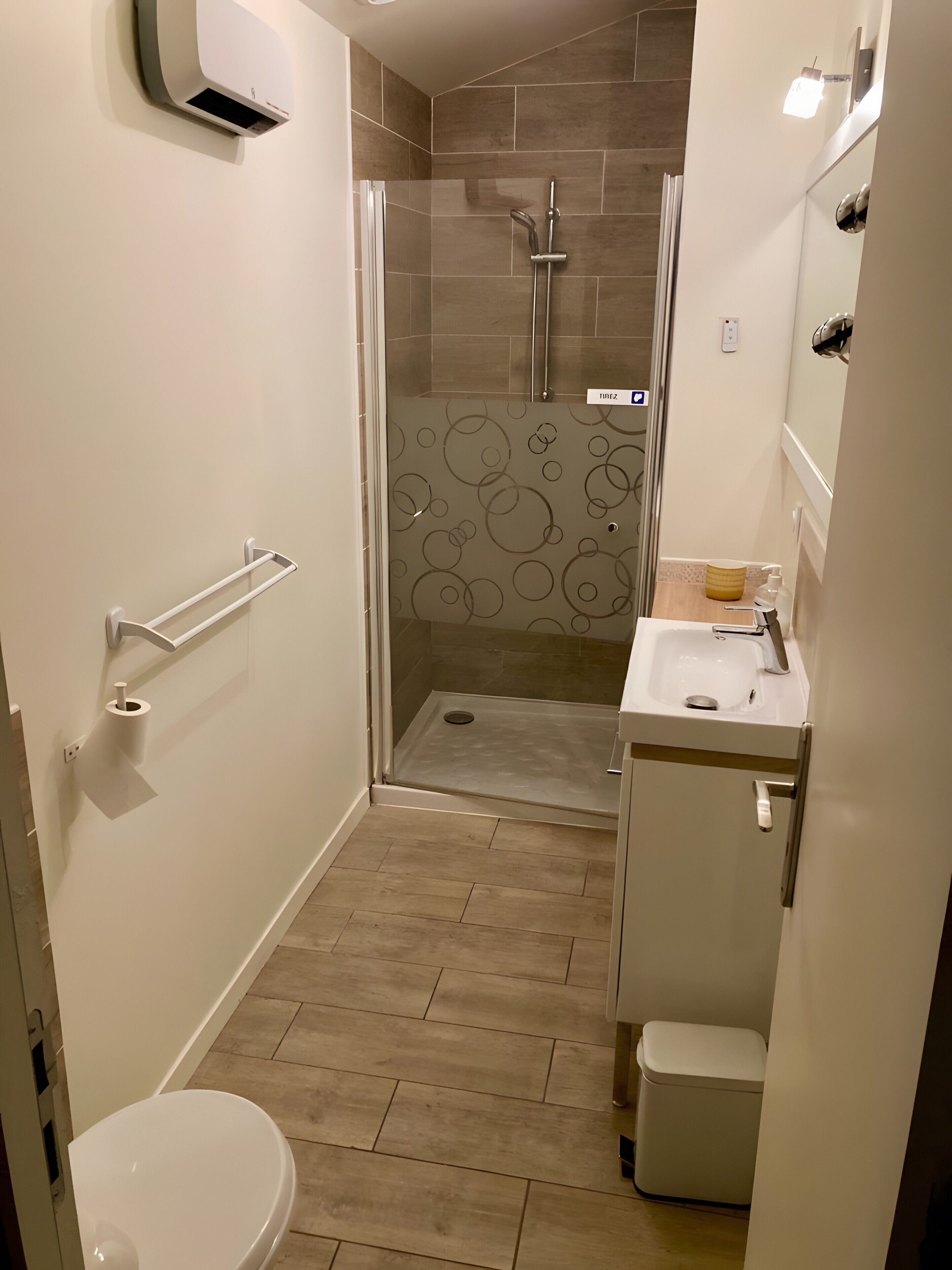 Une salle de bain équipée de toilettes, d’un lavabo, d’une douche et d’une porte en verre.