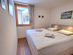 A bedroom with a bed, a window, a wall-mounted lamp, and a painting. - Fewo Cordial im Casa Erizun, (Flims Dorf), by Interhome (Flims)