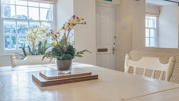 A room with a white table, a potted plant, a door with an exit sign, and a patterned bed. - 7 Grade II Listed Cosy Cottage Free Parking (Ambleside)