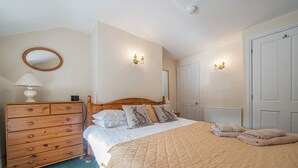 A bedroom with a wooden dresser, a bed with a quilted bedspread, two wall-mounted light fixtures, and a door. - 7 Grade II Listed Cosy Cottage Free Parking (Ambleside)