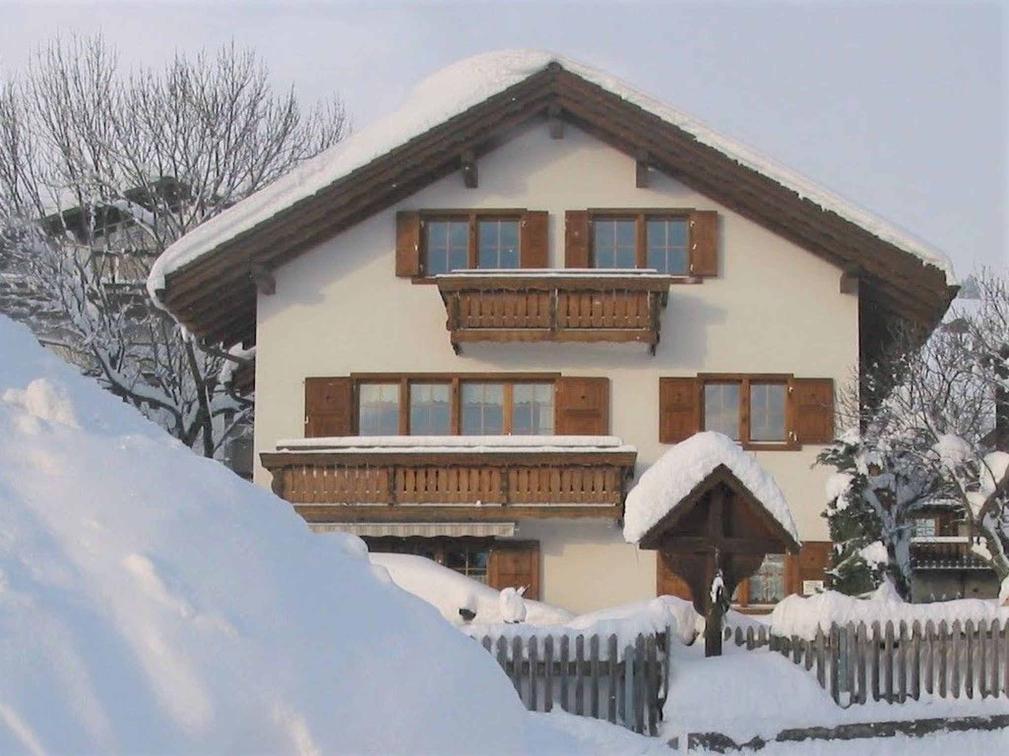 En toetages chalet med træbalkoner og et tag dækket af sne.