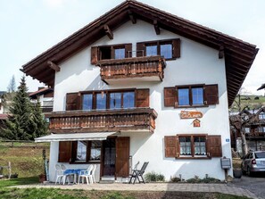 Ein zweistöckiges Gebäude mit hölzernen Balkonen, einem Schild mit der Aufschrift 'Nies Gaglinier' und einem Tisch mit Stühlen vor der Fassade.