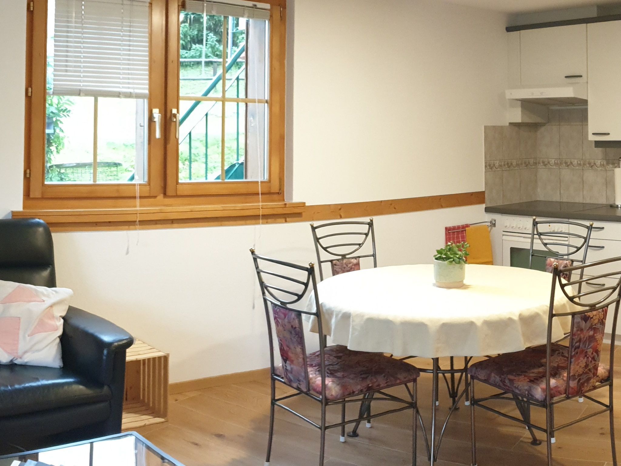 Un coin repas comprenant une table ronde, quatre chaises et une fenêtre donnant sur un paysage verdoyant.