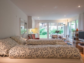 A spacious living room with a large sofa, a dining area with a table and chairs, and a television on a stand. - Grava, (Laax Dorf), 35045 by Interhome (Laax)