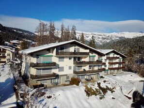 Ein mehrstöckiges Gebäude mit Balkonen, umgeben von verschneiter Landschaft und Bergen.