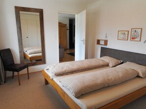 A bedroom with a bed, a chair, a mirror, and a door leading to another room. - Pignia 2 / Greulich, (Laax Dorf), 25223 by Interhome (Laax)