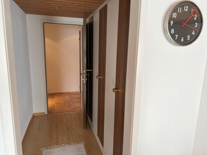 Un pasillo con una puerta de madera, un reloj en la pared y una alfombra en el suelo.