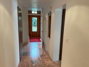 A hallway with a red carpet leading to a wooden door with a window. - Residenza Cristallo, (Flims Dorf), by Interhome (Flims)