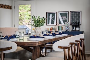Un coin repas avec une table en bois dressée pour six personnes, des chaises, un vase agrémenté de verdure et des œuvres d’art encadrées accrochées au mur.