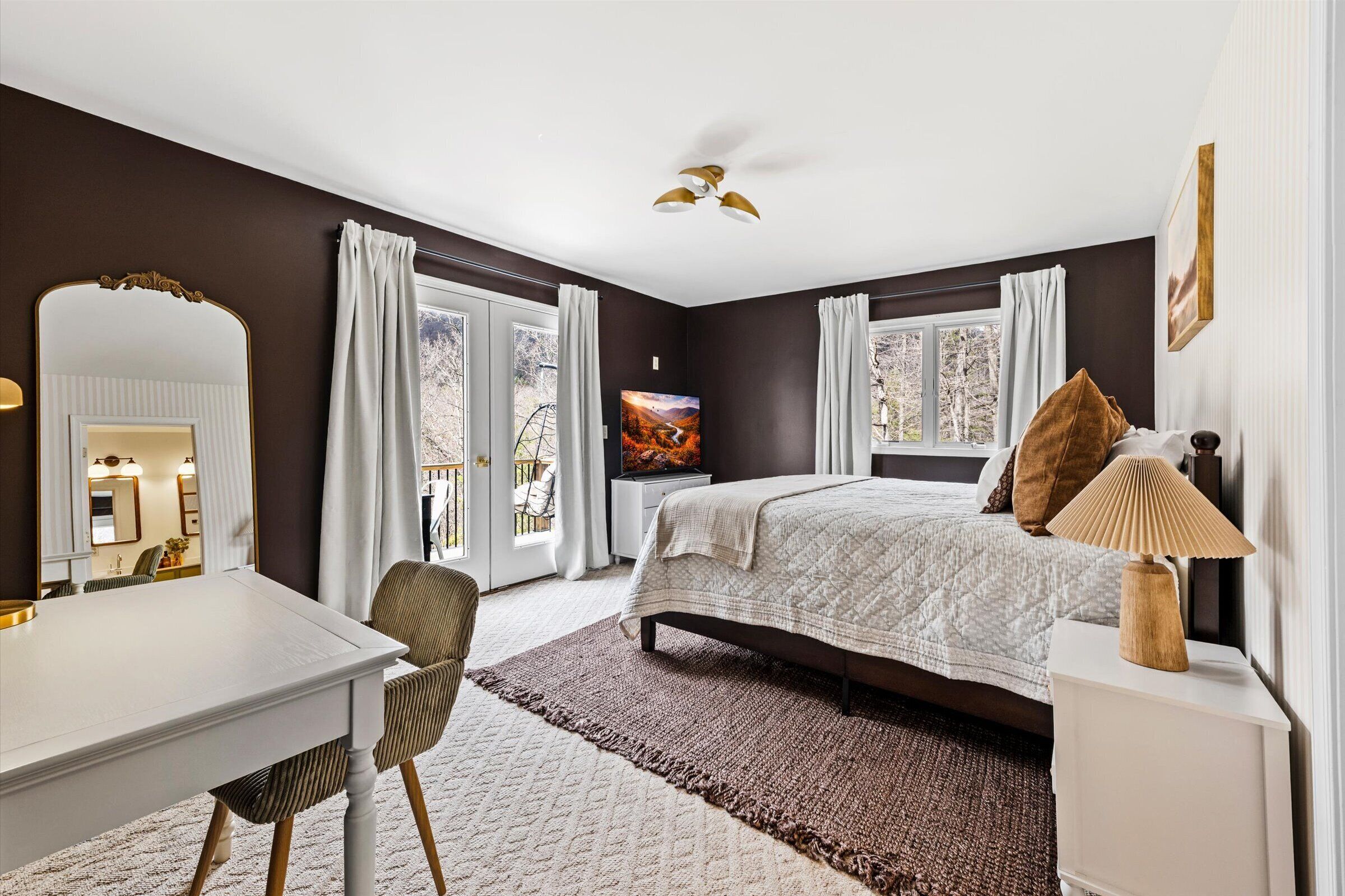 A bedroom with a bed, bedside table, lamp, and a large mirror.