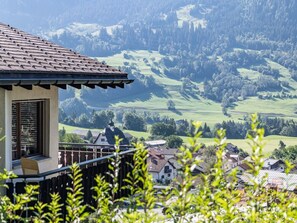 A building with a tiled roof, a balcony, and a view of a green valley with trees and hills. - Mira Piz Mundaun, (Sagogn), 70004 by Interhome (Sagogn)
