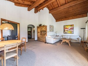 Un vaste espace de vie doté d’un plafond en bois, d’une table à manger avec des chaises, d’un canapé blanc, d’une table basse et d’un meuble.