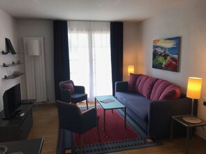 Un salon moderne comprenant un canapé, un fauteuil, une table basse et un téléviseur.