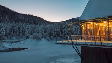 A snow-covered landscape with a building featuring a glass enclosure and interior lighting.