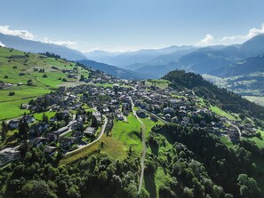 Vista aérea de un pueblo con casas, caminos y colinas verdes circundantes.