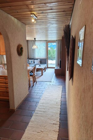 Un pasillo con techo de madera, alfombra, sofá y mesa de comedor.