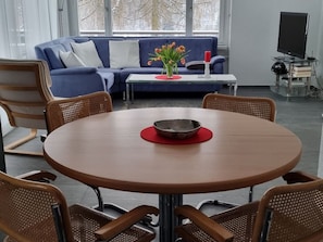 A modern living room with a round wooden table, wicker chairs, a blue sofa, and a glass coffee table. - Casa Marcau, (Flims), by Interhome (Flims)