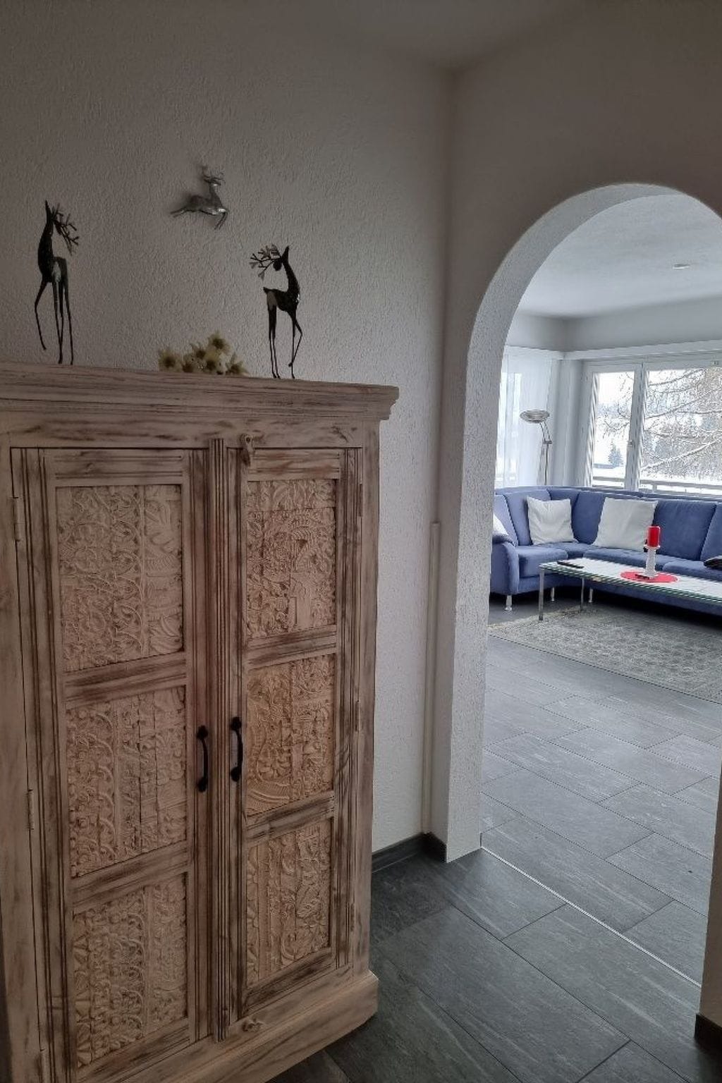 A room with a large wooden cabinet, a sofa, and a view through an archway to a balcony.