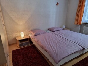 A single bed with a red rug, a bedside table with a lamp, and a window with curtains. - Casa Marcau, (Flims), by Interhome (Flims)