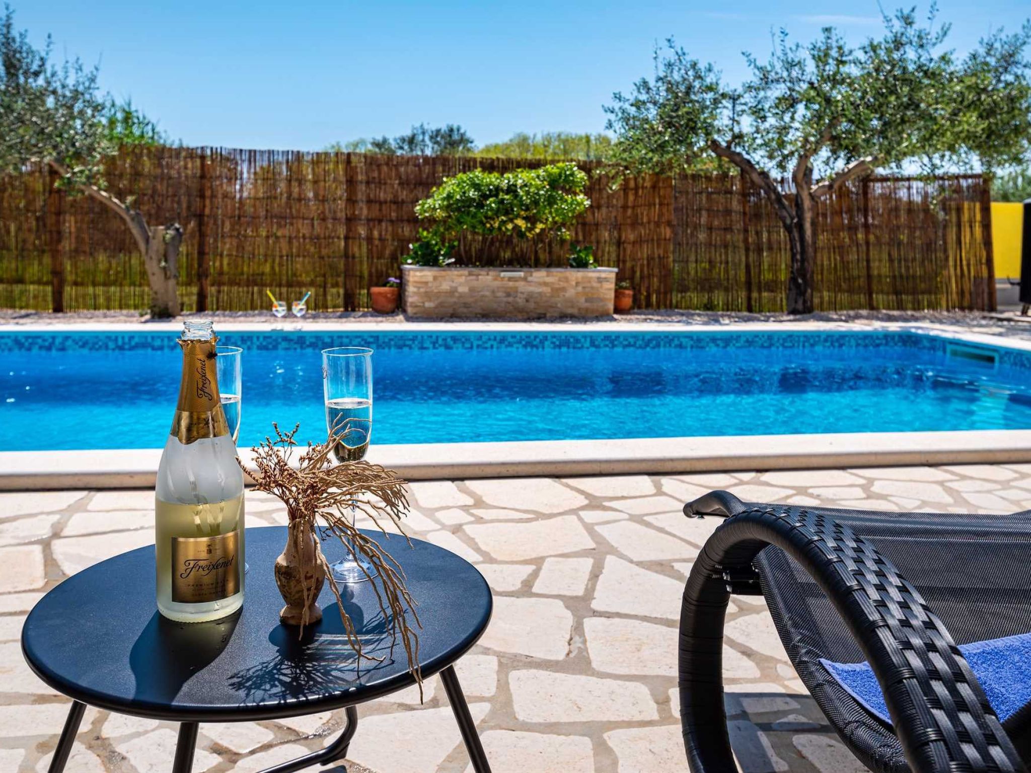 Escena junto a la piscina con una mesa, una botella y vasos.
