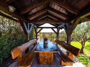 An outdoor wooden pavilion with a table and benches, surrounded by greenery. - Apartment house Simoni with pool by Interhome (Privlaka)