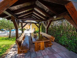 An outdoor wooden pavilion with a bench and picnic table, surrounded by greenery. - Apartment house Simoni with pool by Interhome (Privlaka)