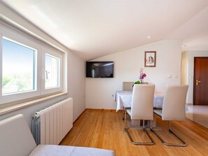 A modern, well-lit room with a large window, a flat-screen TV mounted on the wall, a dining table with chairs, and a radiator. - Apartment house Simoni with pool by Interhome (Privlaka)