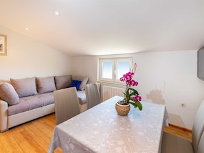 Una sala de estar acogedora con un sofá, una mesa con un jarrón de flores y una ventana con persianas.