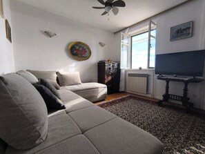 A living room with a sofa, a television, a radiator, and a window. - House Deša with amazing Old Town and sea view (Dubrovnik)
