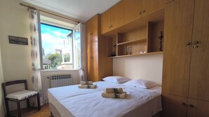 A bedroom with a bed, a chair, wooden cabinets, and a window with a view. - House Deša with amazing Old Town and sea view (Dubrovnik)
