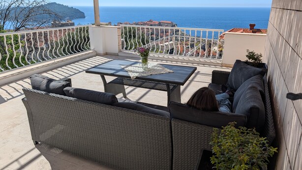 A balcony with wicker furniture, a glass-top table, and a view of the sea. - House Deša with amazing Old Town and sea view (Dubrovnik)