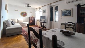 A living room with a sofa, a dining table, a TV, and a radiator. - House Deša with amazing Old Town and sea view (Dubrovnik)