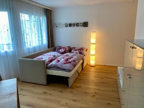 A bedroom with a bed, a bedside table, a lamp, and a window with curtains. - Casa Primavera B21, (Flims Dorf), by Interhome (Flims)