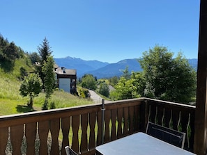 Uma varanda com mesa e cadeiras, com vista para uma paisagem montanhosa sob um céu limpo.