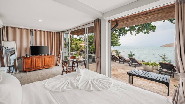 Ein Hotelzimmer mit einem großen Bett, einem Fernseher, einem Holzschrank, einem Esstisch und Blick auf den Strand.
