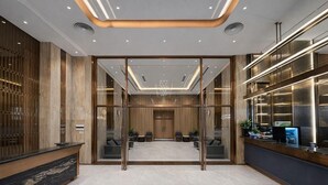 Eine moderne Hotelhalle mit Empfangstresen, Sitzgelegenheiten und einer Glastrennwand.