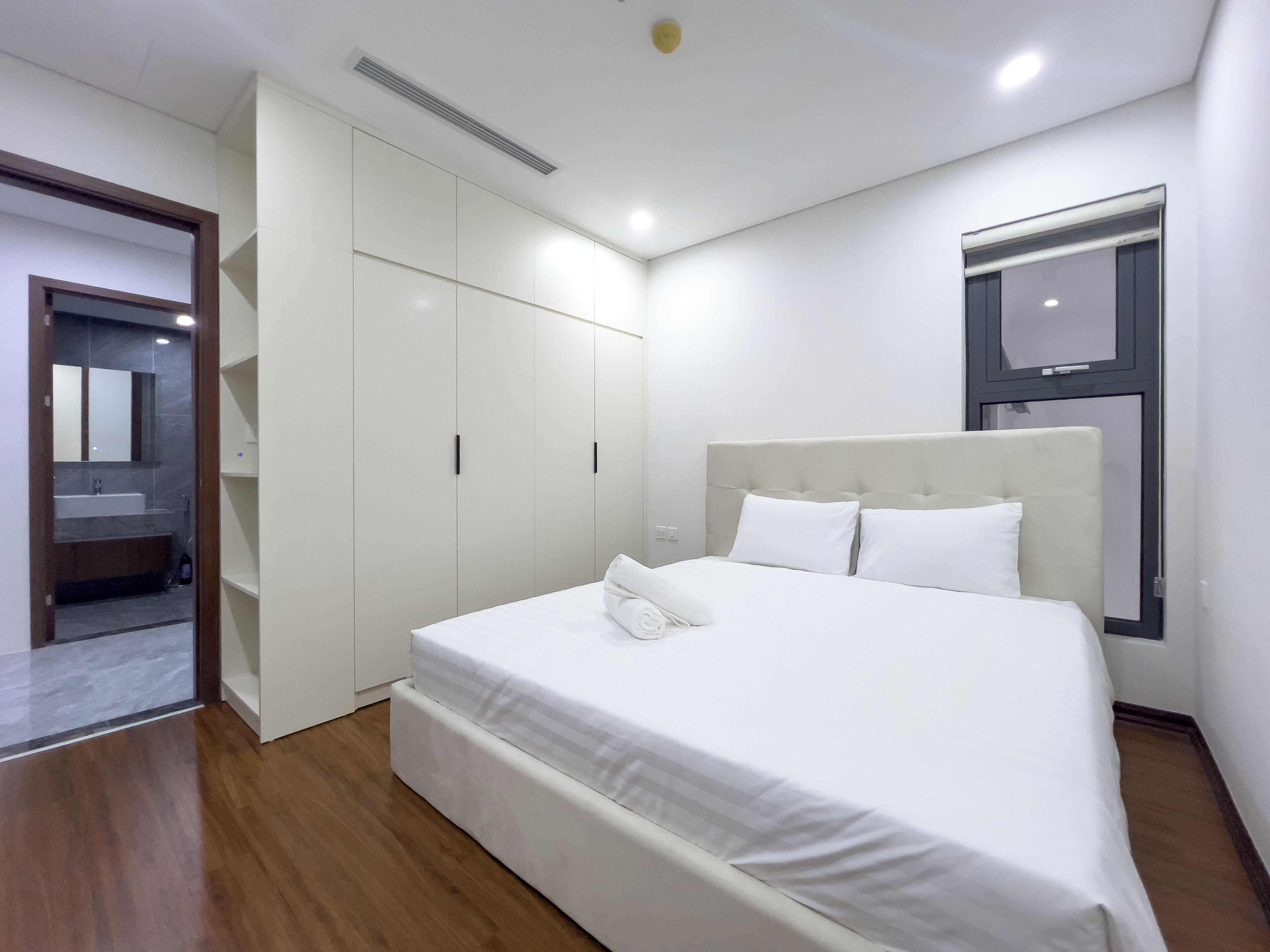 A modern bedroom with a large bed, built-in wardrobe, and a bathroom visible through an open door.