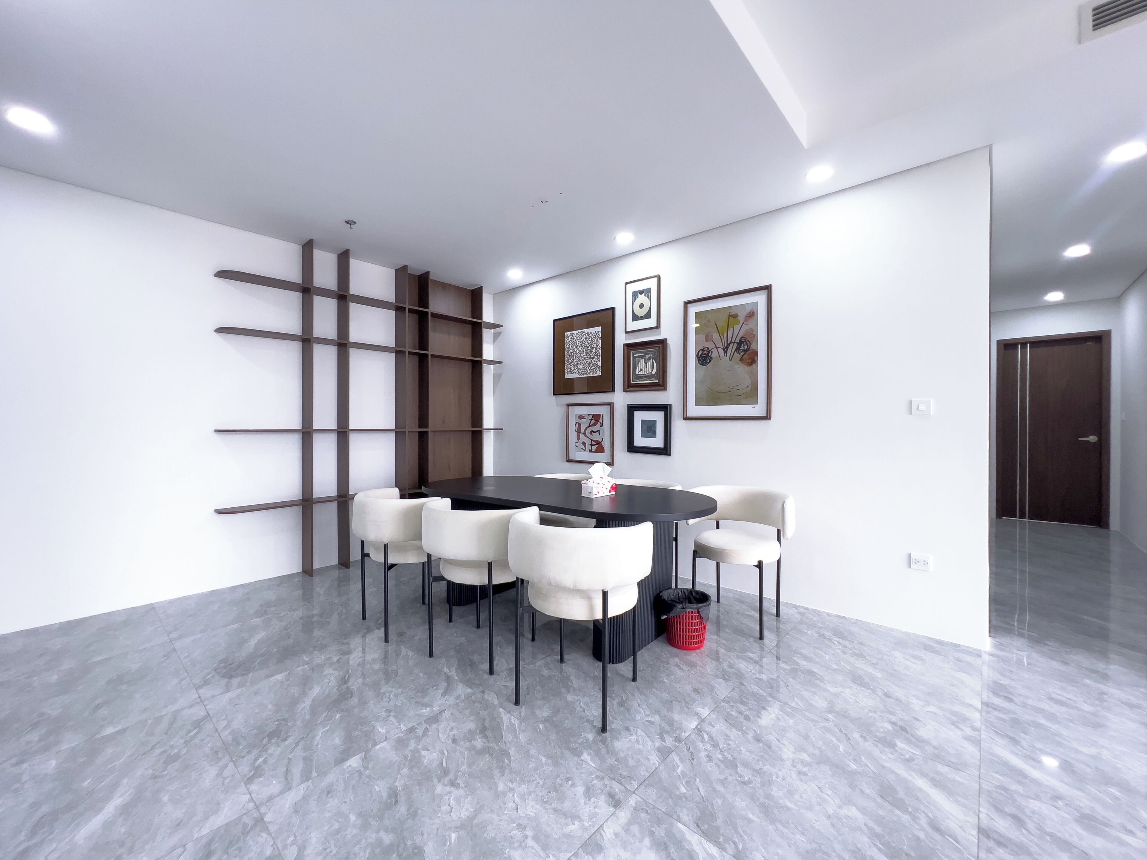 A modern conference room with a round table, white chairs, a black trash bin, and framed artwork on the wall.
