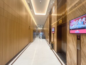 A modern hotel corridor with wooden paneling, a digital screen displaying a TV show, and a marble floor. - Capital Elite Luxury Residences (Ha Noi)