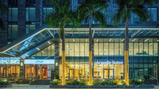 Ein Hotel mit moderner Glasfassade, Palmen und einem Schild für 'Aravelle Suites'.