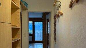 Um corredor com estantes de madeira, tapete, cabideiro na parede e porta que dá para uma varanda.