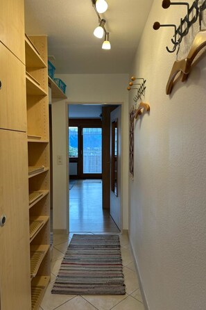 Ein Flur mit Holzböden, einem Teppich, einem Wandhaken für Kleidung und einer Tür zu einem Balkon.