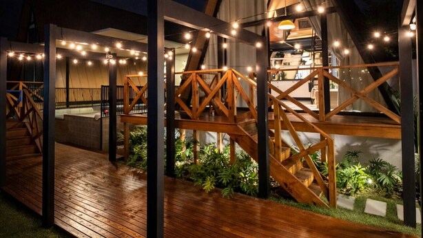 A modern building with a wooden deck, a glass facade, and string lights. - Cabana com Piscina Aquecida e Spa (Palhoça)