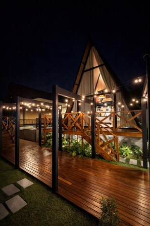 A modern building with a wooden deck, a glass facade, and string lights.