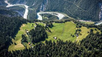 An aerial view of a mountainous landscape with a river, forested areas, and scattered buildings.
