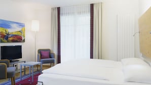 Ett hotellrum med en säng, en tv, en stol, ett litet bord och en tavla på väggen.