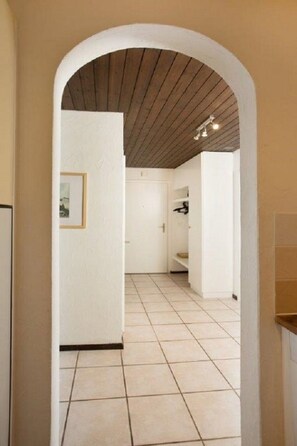 A hallway with a tiled floor, a wooden ceiling, and white walls. - Apartment  by Interhome (Laax)