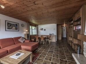 A cozy living room with a sofa, a dining table with chairs, and a kitchen area with wooden cabinets and a tiled floor.