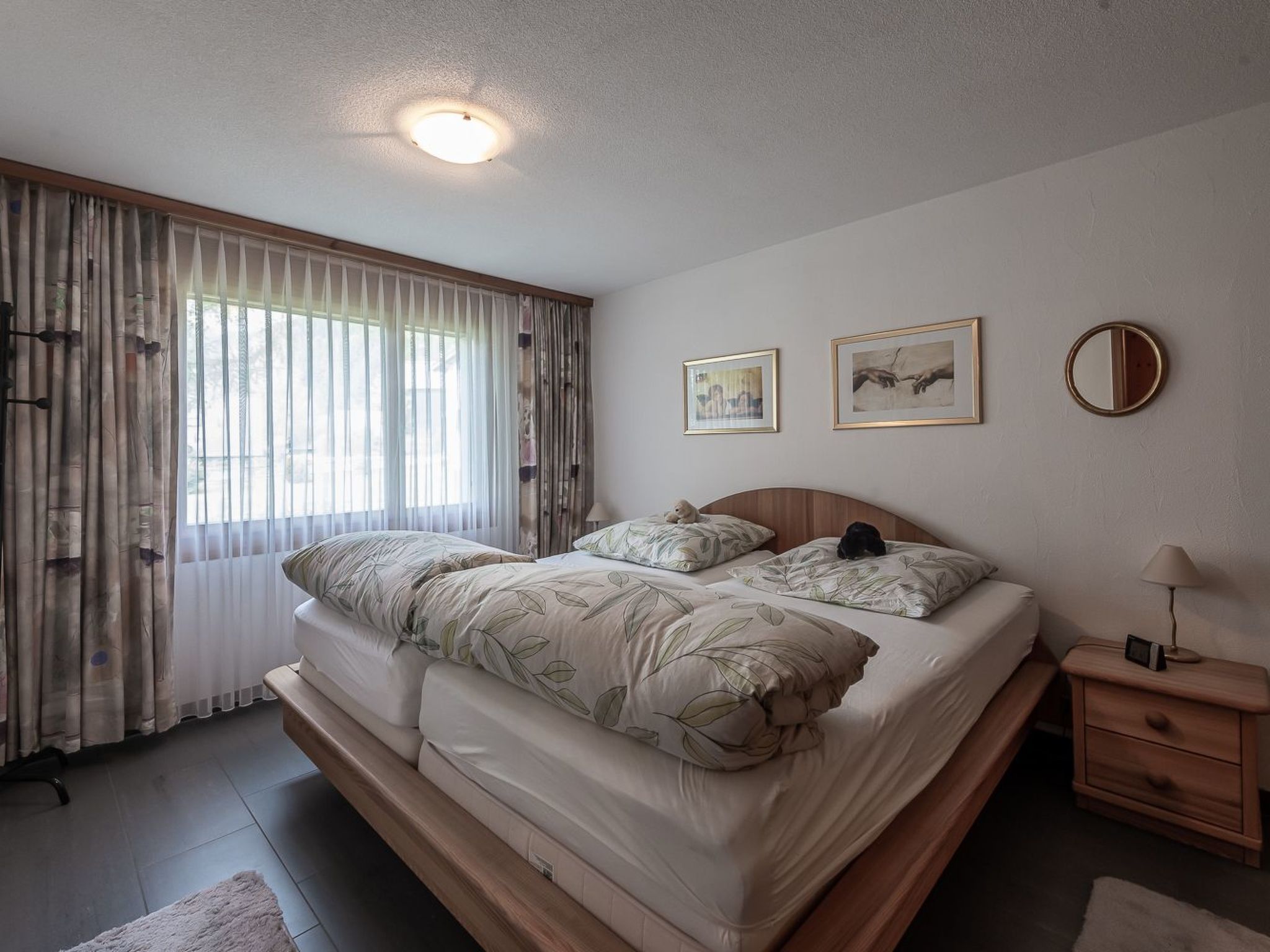 A bedroom with a bed, a nightstand, a lamp, and two framed pictures on the wall.