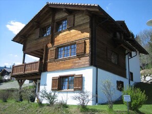 Ein zweistöckiges Holzhaus mit einem Balkon, einem weißen unteren Bereich und einer Steinsäule.